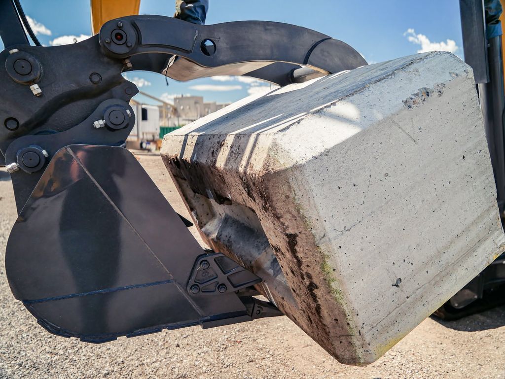 Excavator bucket and thumb gripping a concrete block